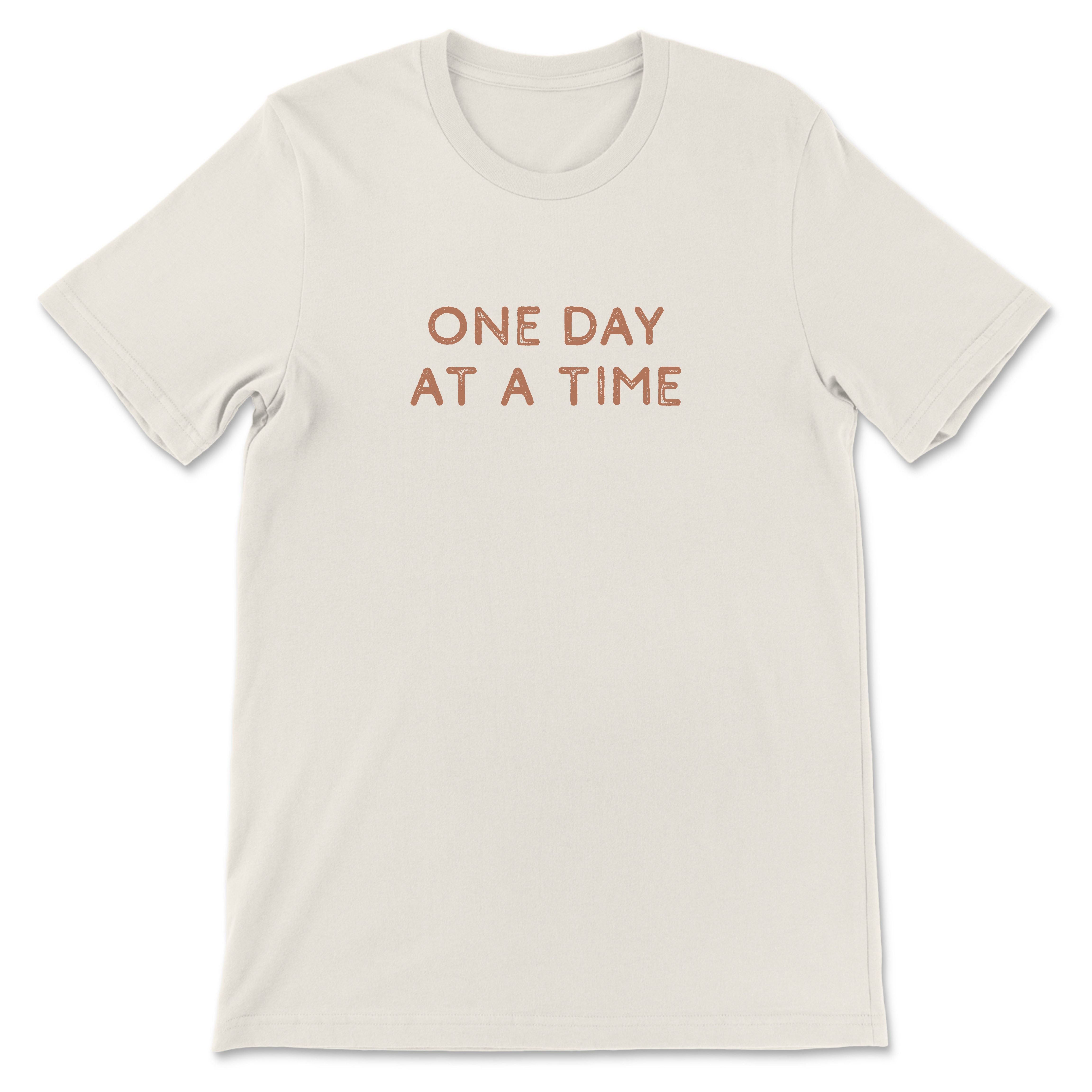 Neutral toned tee with take it one day at a time printed on back, styled casually for an everyday look