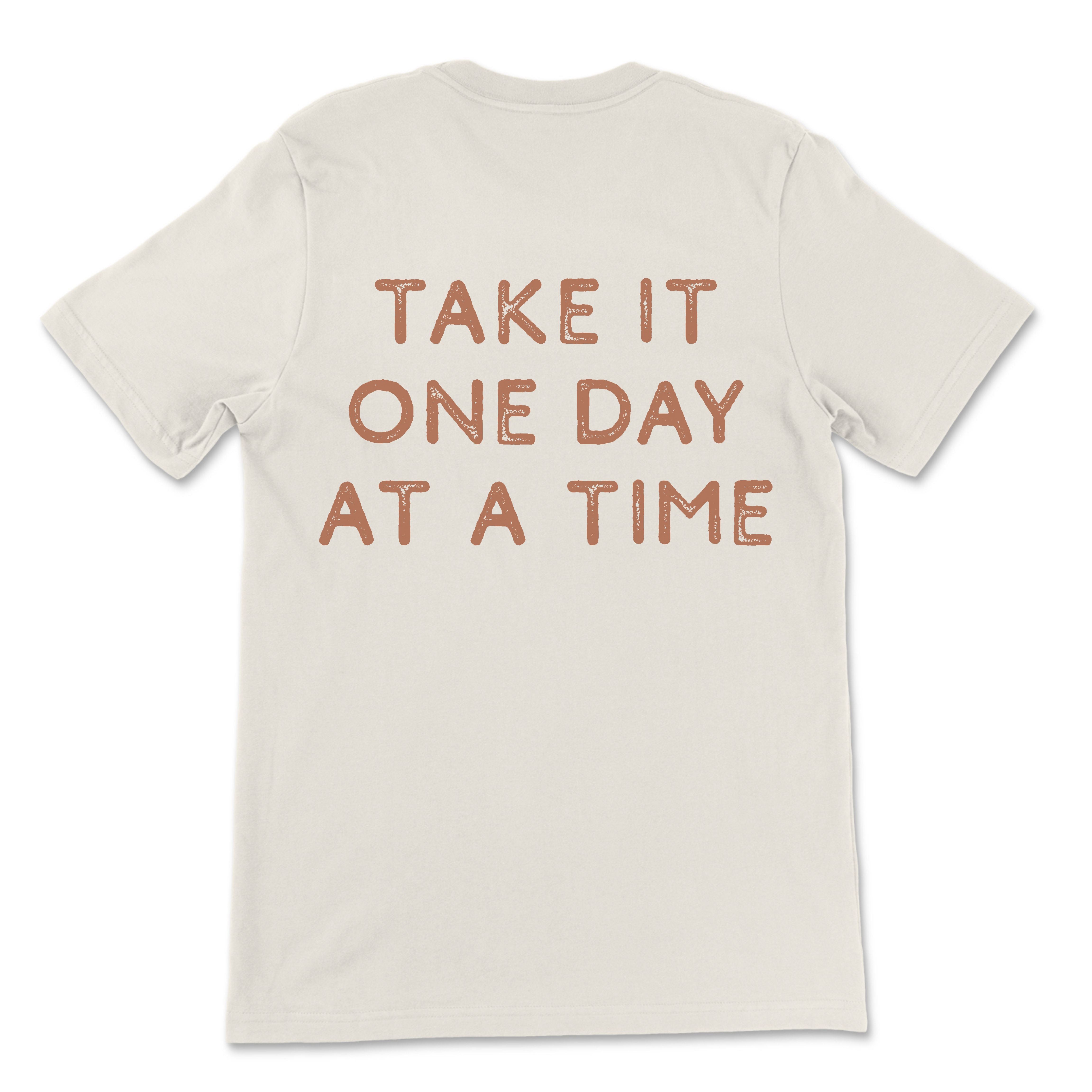 Neutral toned tee with take it one day at a time printed on back, styled casually for an everyday look