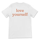 Natural tee with small “be kind” text on front chest and bold “love yourself” text across back
