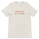 Neutral toned tee with take it one day at a time printed on back, styled casually for an everyday look